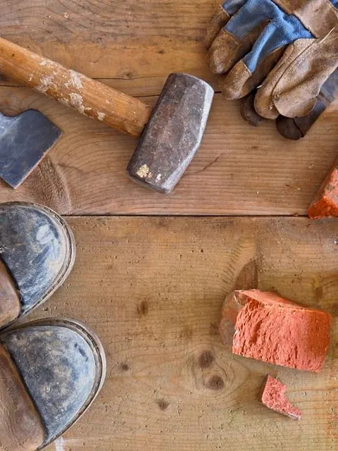 Outils de maçon sur du bois : masse, gants et morceaux de brique
